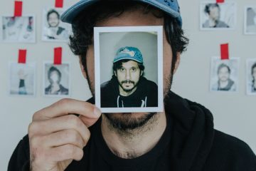 Portrait of Yoni Wolf holding a photo of himself in front of his face.