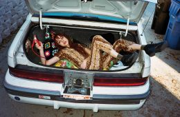 Woman laying in trunk of car in a Rusty Cuts jumpsuit.