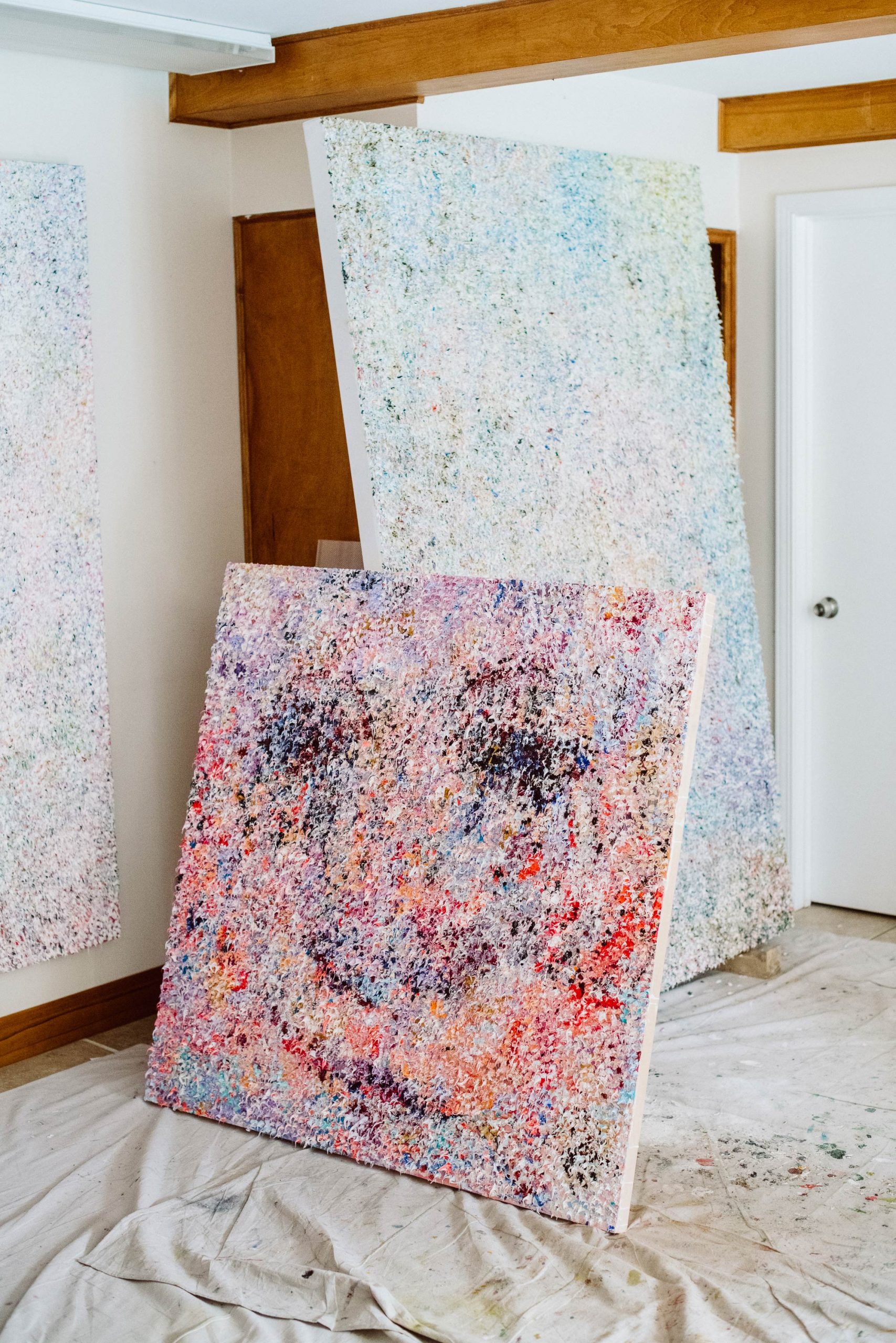 A small painted canvas leaning up against two larger white painted canvases.