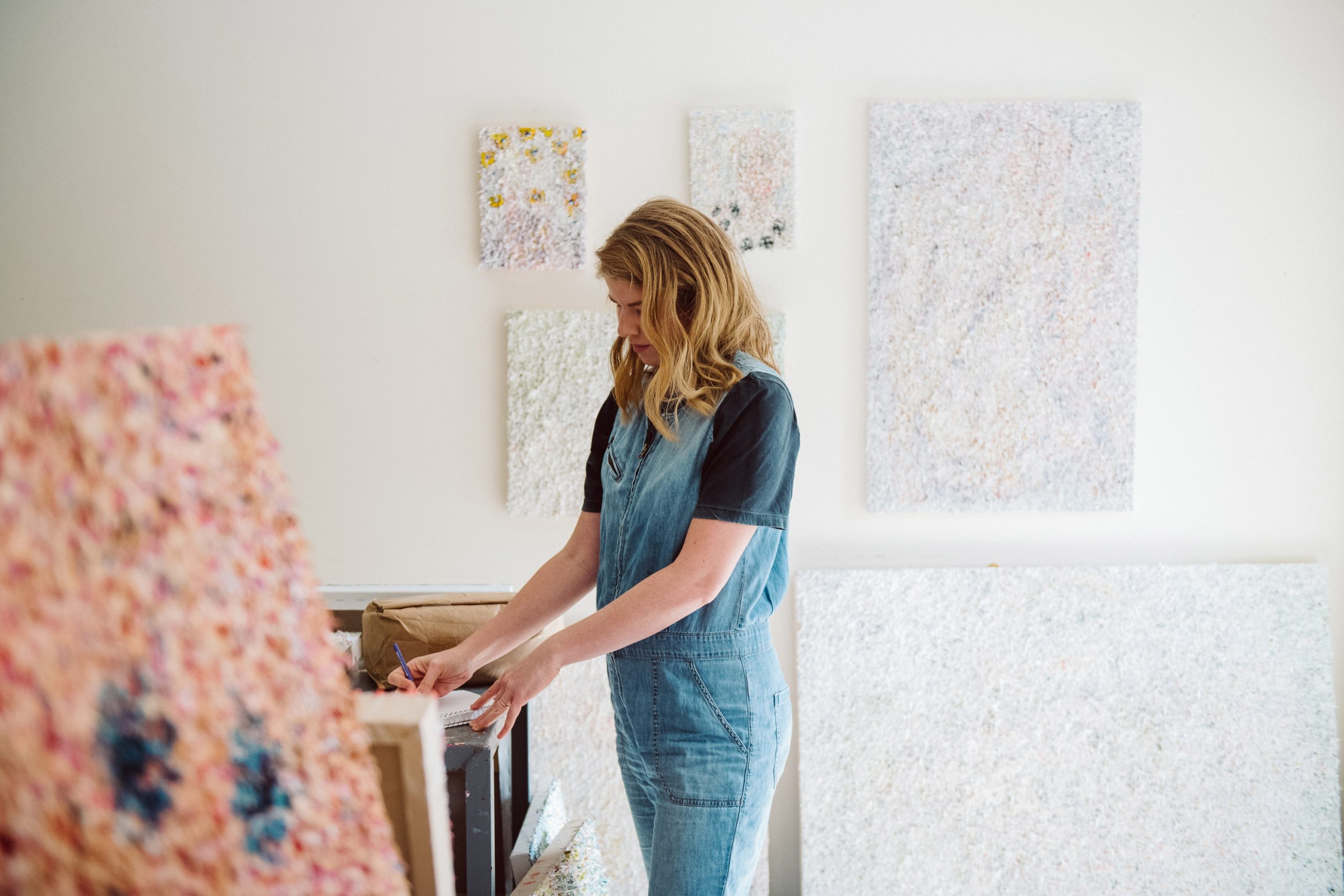 Vanessa standing over a studio table, sketching in a notebook.