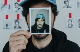 Portrait of Yoni Wolf holding a photo of himself in front of his face.