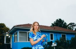 Singer Julia Jacklin wearing a blue dress and standing in front of a blue house.